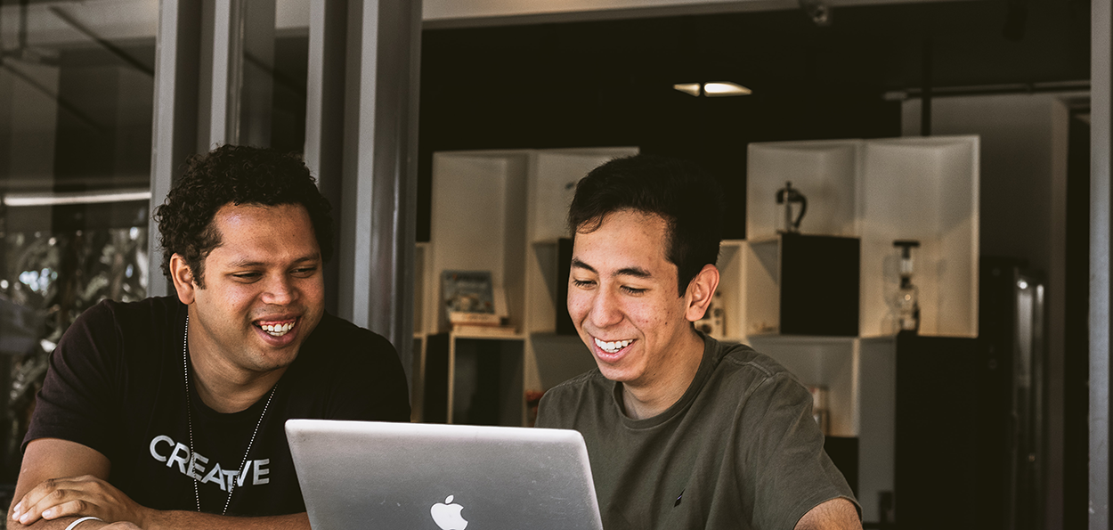 Två unga män samarbetar och ler vid laptop